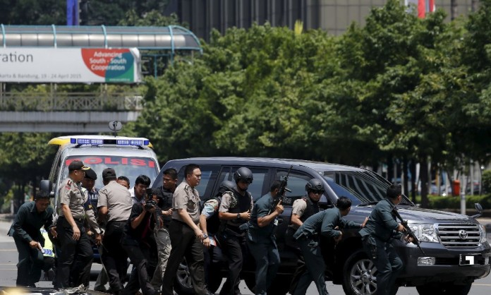 Dead bodies are seen as Indonesian police hold rifles while walking behind a car for protection in Jakarta