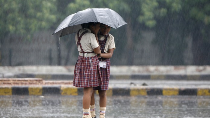 Schoolgirls stand on a road divider as they huddle under an umbrella during monsoon rain in New Delhi monsoon strengthen kerela within 2 days