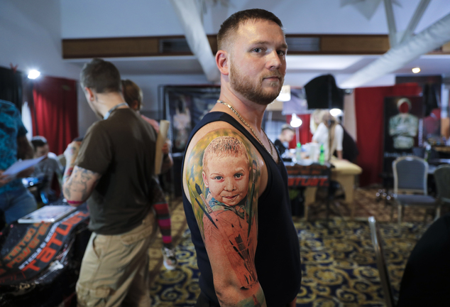 In this picture taken on Sunday, Oct. 16, 2016, Serghei, from the Republic of Moldova, poses with a fresh tattoo showing his son Chiril applied to his hand, during the International Tattoo Convention Bucharest 2016 in Bucharest, Romania. (AP Photo/Vadim Ghirda)