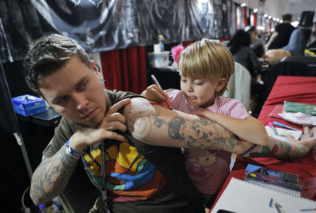 In this picture taken on Sunday, Oct. 16, 2016, Ave, 4 year-old from the United States, paints on her father's arm during the International Tattoo Convention Bucharest 2016 in Bucharest, Romania. More than 100 tattoo and piercing artists brought their skills and art to a three-day convention in the Romanian capital.(AP Photo/Vadim Ghirda)