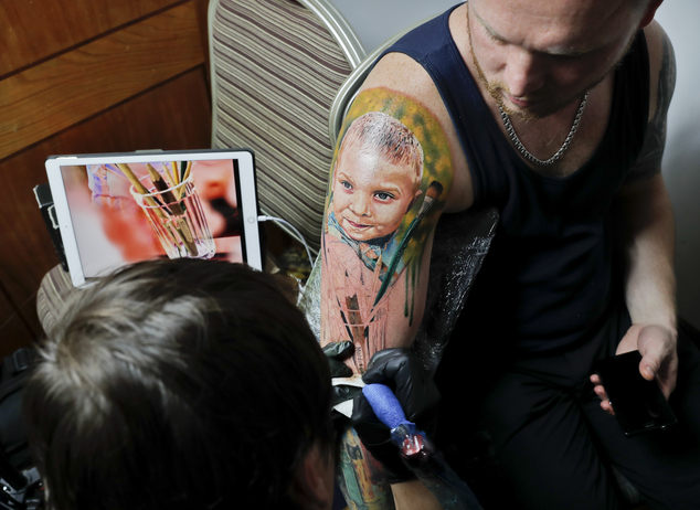 In this picture taken on Sunday, Oct. 16, 2016, Serghei, from the Republic of Moldova, gets a tattoo showing his son Chiril applied to his hand, during the International Tattoo Convention Bucharest 2016 in Bucharest, Romania. (AP Photo/Vadim Ghirda)